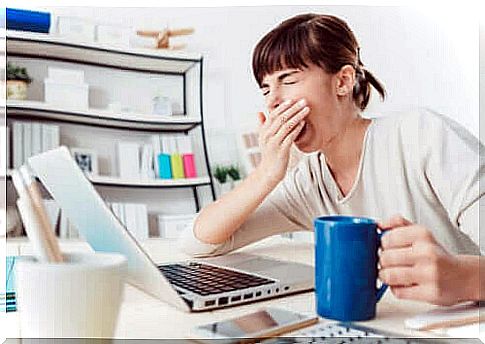 Woman at desk yawns due to sleep inertia